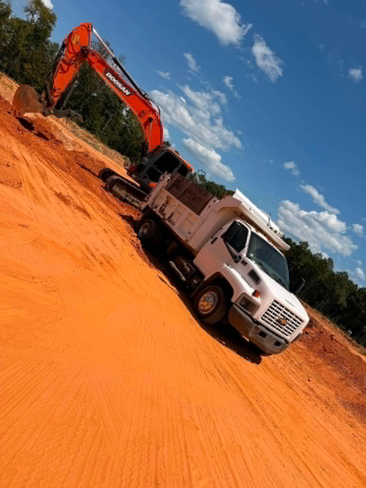 Excavator loading a Saline County Gravel dump truck on a fresh red clay pad